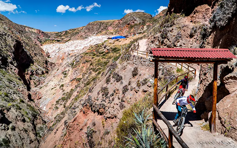 Cyclist riding near wooden rooftops and salt pools of Maras, approaching the iconic mines (Peru Biking Tours)
